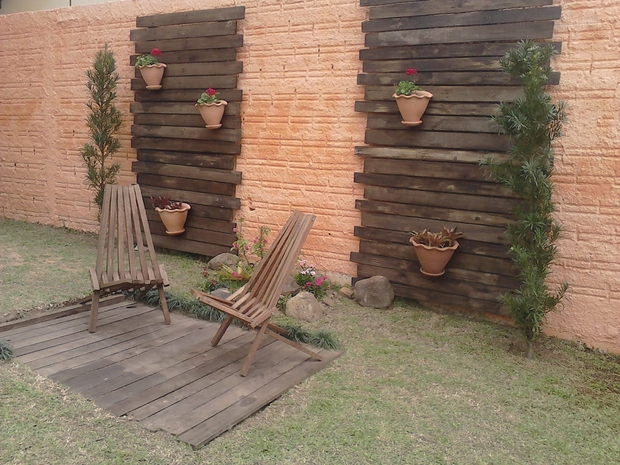 vertical garden pallet wooden slats varnished armchairs flower pots bricks wall backyard lawn